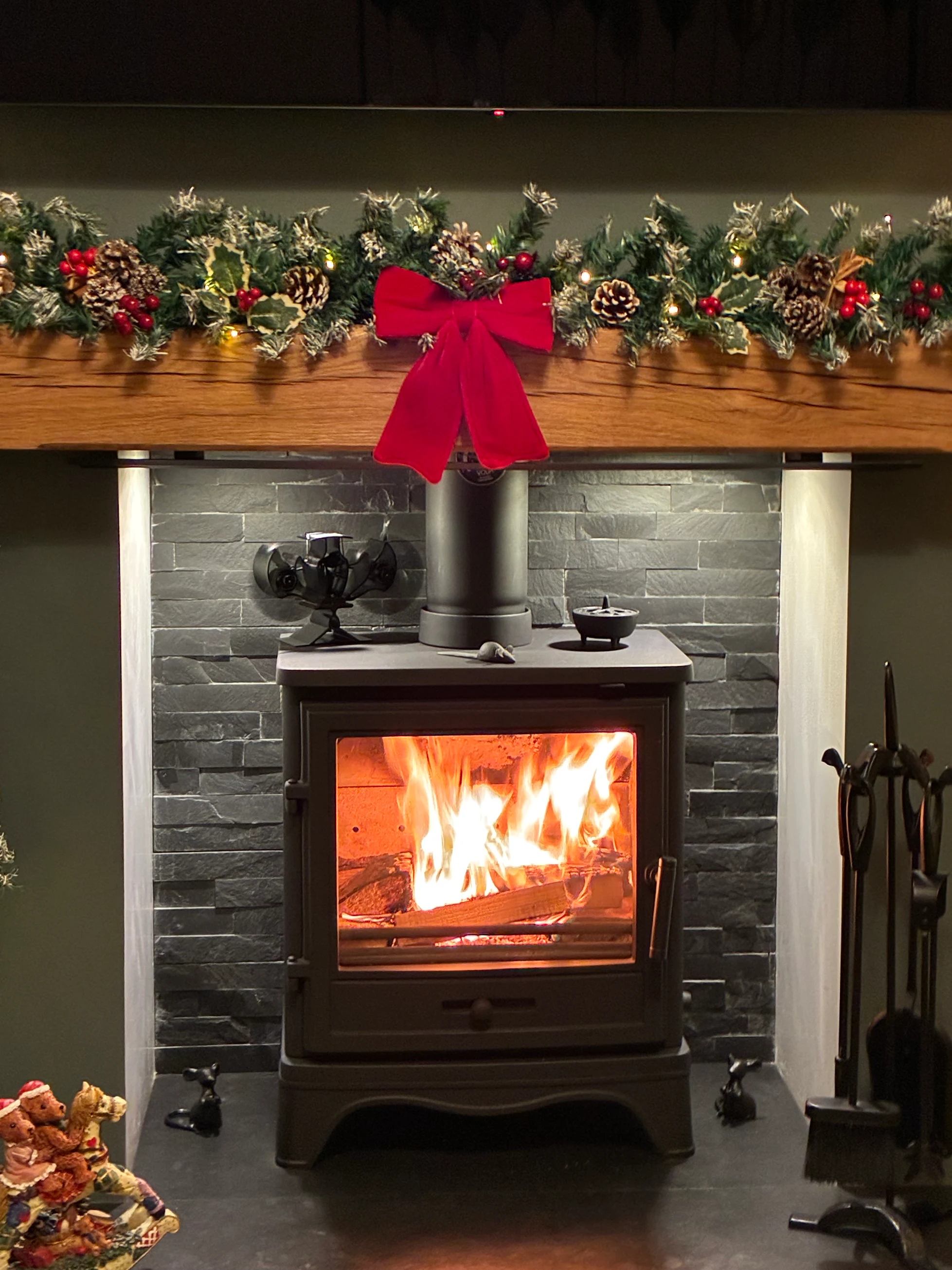 A traditional wood burning stove lit in a split-slate chamber with a solid oak beam mantel